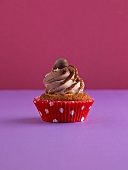 A cupcake on a purple surface against a pink background