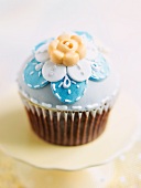 A cupcake decorated with blue icing and a sugar flower