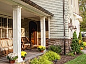 Sonnige Veranda mit gemütlichen Korbmöbeln neben der Eingangstür eines schindelbedeckten Hauses