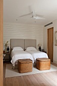 Twin beds with tall, upholstered headboards and two large wicker trunks at foot