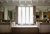 Marble bathtub below half-closed window shutters in spacious bathroom