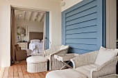 Bequeme Balkonmöbel mit Fussschemel und Tabletttisch vor blauer Wand und Blick ins Schlafzimmer durch die geöffnete Schiebetür