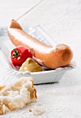 A hot dog sausage with mustard, a tomato and bread