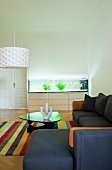 Schlichtes Sofa übereck und Klassiker Couchtisch auf Streifenteppich in minimalistischem Wohnzimmer