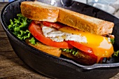 Sandwich mit Ei, Tomaten, Salat und Speck in einer Pfanne