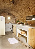 Bathroom with stone walls, wooden cupboard doors in concrete washstand and concrete floor with pebble border