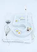 Floating daisies and lit birthday candle in white china dish in the shape of a number