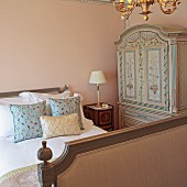 Patterned scatter cushions on antique sleigh bed and wardrobe painted with floral motifs in corner of bedroom