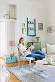 Young woman seated in comfortable living room with vintage furniture, knitted rug and striped wallpaper