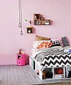 Bed with storage compartments below, small decorative shells on wall and industrial pendant lamps above bedside cabinet in jaunty pink
