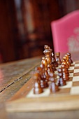 Wooden chess pieces on chessboard on old table with blurred pink chair in background (Schloss Schauenstein)