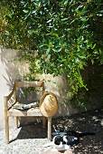 Sunhat hanging on simple wooden armchair next to cat sitting on floor of terrace