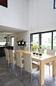 Dining chairs with pale covers and minimalist dining table in pale wood in front of terrace window in contemporary house