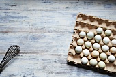 Fresh Pastel Colored Eggs in a Cardboard Carton on a Wooden Table; From Above