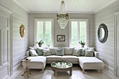 Comfortable sofa combination with two chaise elements in wood-panelled living room with chandelier and round mirrors