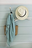 Summer hat, scarf and bag hanging on nostalgic coat pegs on pale blue wall panelling