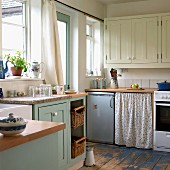 Country-house style kitchen-dining room with cream and pastel blue fronts, retro fridge and floral curtain