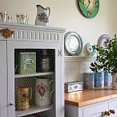 Old, white-painted china cupboard with wire mesh door panel and romantic, floral crockery decorating country-house kitchen