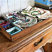 Tablett mit Schachteln voller bunter Perlen und Ketten auf altem Holzschrank