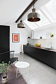 Monolithic kitchen counter with black fronts below strip of skylights and metal, industrial-style pendant lamps