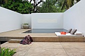 Geometrischer Poolbereich mit Liegepolster und Kissen zwischen weißen Wänden von Bäumen überragt, strahlt Ruhe und Klarheit aus