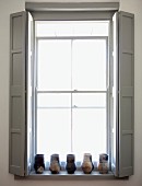 Window with pale grey interior shutters and collection of vases on windowsill