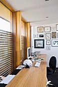 Picture gallery at the end of a writing desk in front of a wall of windows with built in blinds