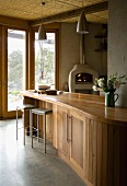 Geschwungene Küchentheke aus Holz und filigrane Barhocker vor Terrassenfenster mit Ausblick in Garten