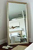 Full-length, silver-framed mirror in elegant bedroom with striped bed headboard and modern painting