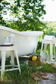 Toiletries on stool next to free-standing vintage bathroom in green landscape