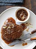 Steak with Peppercorn Sauce and Shallots on a White Plate with a Fork and Knife