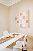 Dining table and white shell chairs in front of modern artwork on beige-painted wall
