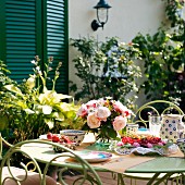Kaffeeservice aus Keramik und blauem Muster und Gartenstrauss auf Tisch vor Wohnhaus mit geschlossenen, grünen Fensterläden