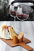 A cheeseboard with grapes and two glasses of red wine