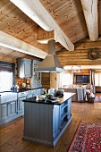 Country-house kitchen with central island counter and wooden fronts painted pale grey in open-plan interior of log cabin