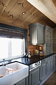 Base units and wall cabinets with wooden doors painted pale grey in country-house kitchen in log cabin