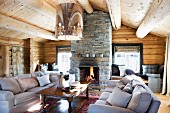 Comfortable sofa set and wooden coffee table below modern, retro ceiling light in log cabin interior with open fireplace