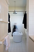 Radiator with towel rails and free-standing bathtub; dark articles of clothing hanging on metal rod