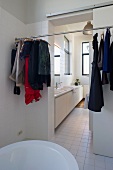 Various items of clothing hanging from rod and view of long washstand in adjacent room
