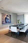 Weissbezogene, gepolsterte Stühle an hellgrauem Tisch gegenüber grossformatigem Bild an grauer Wand in modernem Esszimmer