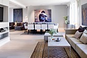 Moderne Loungeecke vor Essplatz mit weissen, gepolsterten Stühle und grossformatiges Bild an grauer Wand in offenem Wohnraum