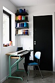 Work area - knitting machine on table with 50s-style chair next to wall-mounted shelves holding spools of brightly coloured yarn