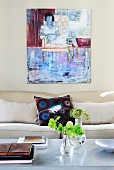 Flowers on coffee table in front of modern sofa and painting on pale grey wall