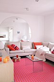 Large, round mirror on wall behind corner sofa and plexiglass table on pink rug