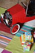 Blick auf rotes Kinderfahrzeug im Vintagestil und Spielzeug auf gestreiftem Teppichläufer