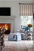 Upholstered armchair and footstool next to blazing open fire