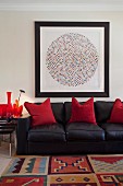 Black leather sofa with red, decorative pillows under an abstract painting