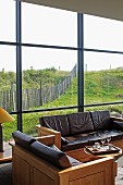 Sofa set of cubic wooden elements with leather cushions; glass wall with view of meadow landscape