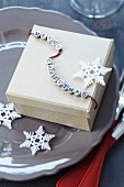 Festive gift box with string of lettered beads reading 'Merry Christmas' and stylised snowflakes