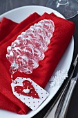 Weihnachtliche Tischdeko mit Tannenzapfen aus Glas und Papieranhänger auf roter Leinenserviette